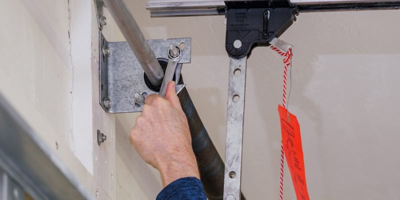 Man repairing electric garage door coiled tension spring. Installing and adjusting overhead garage door opener.
